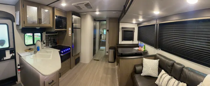 Inside a modern rv rental: kitchen with sink & stove, dinette, and living area with comfy sofa. Hallway leads to rear.. Keystone RV Hideout 2021