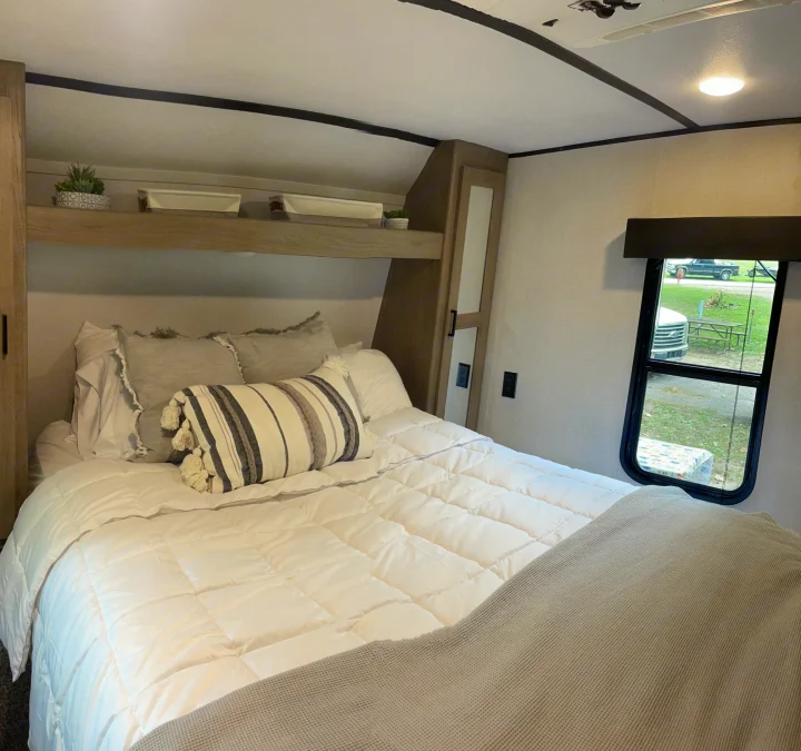 Spacious RV rental bedroom featuring white bedding, overhead storage, and a scenic campsite view from the window.. Keystone RV Hideout 2021