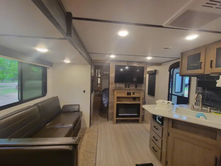 Spacious RV rental interior featuring a comfy sofa, wall-mounted TV over a fireplace, and modern kitchen island.. Keystone RV Hideout 2021