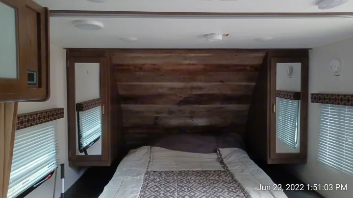 Cozy RV rental bedroom showing a bed, rustic wood headboard, and mirrored side wardrobes.. Keystone RV Passport Express 2019