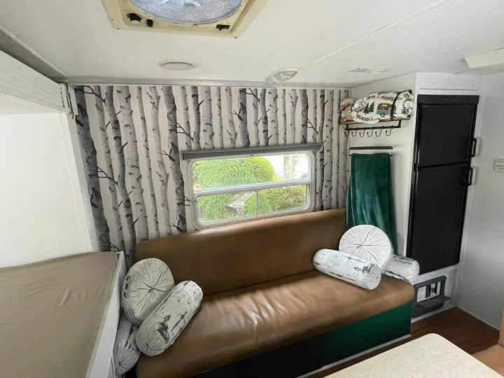 Cozy RV rental interior featuring birch wall decor, brown leather couch, log pillows, and a built-in fridge.. Forest River Surveyor 2006