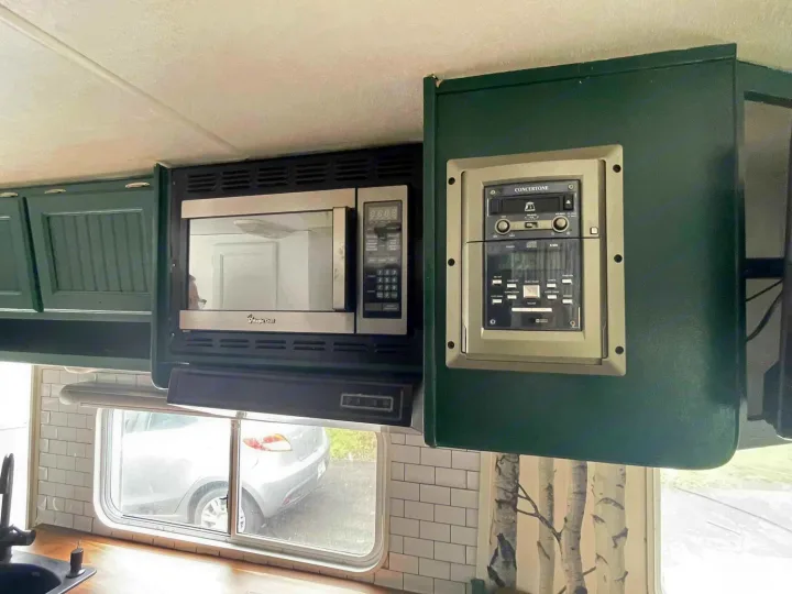 Inside an RV rental: dark green cabinets, built-in microwave, and Concertone stereo above a tiled kitchen area.. Forest River Surveyor 2006