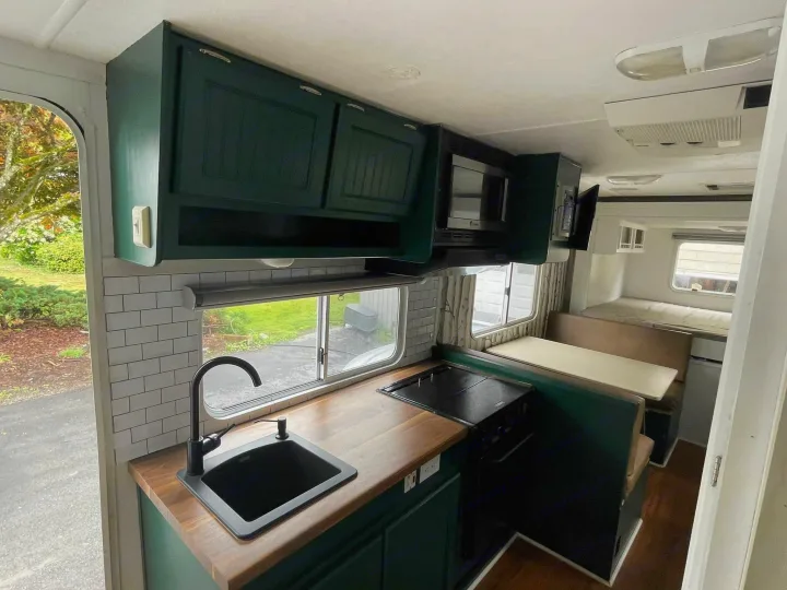 Modern RV rental kitchen: dark green cabinets, wood countertops, black sink, and a convertible dinette area.. Forest River Surveyor 2006