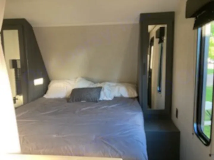 Step inside this cozy RV rental bedroom. Features a queen bed, mirrored storage cabinets, and a window for natural light.. Dutchmen Other 2022