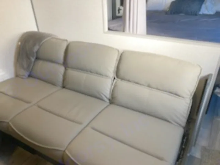 This RV rental features a sleek, grey sofa, ideal for relaxing in the living space. Bedroom visible through opening.. Dutchmen Other 2022