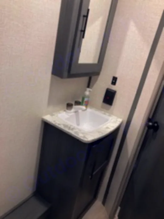 Compact RV rental bathroom features a grey vanity with a white sink and mirror cabinet, ideal for travel.. Dutchmen Other 2022