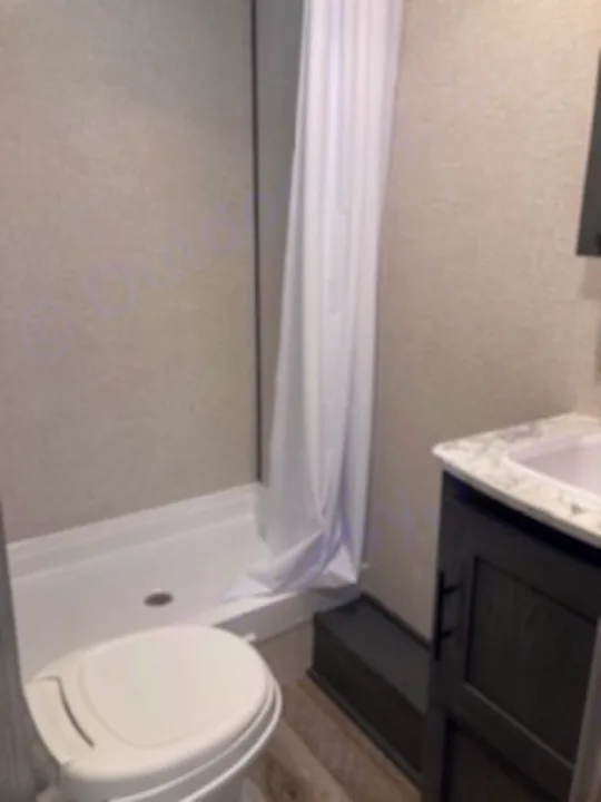Compact RV rental bathroom: A white toilet, shower with white curtain, and dark vanity with a white sink are visible.. Dutchmen Other 2022