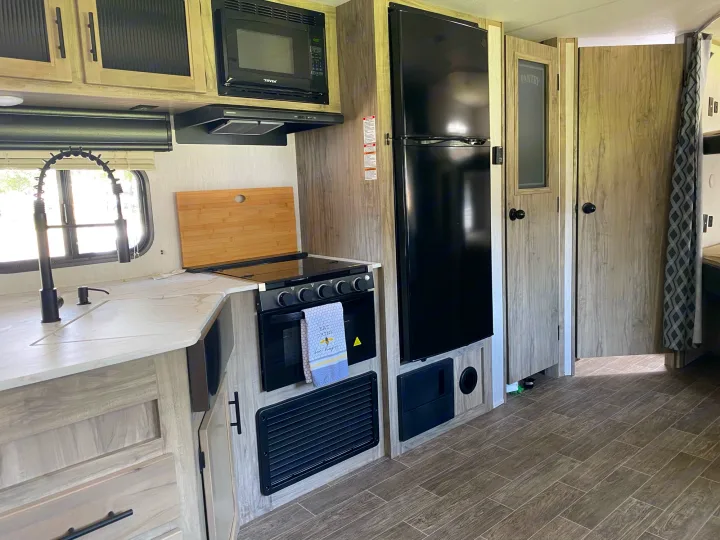 Modern RV rental kitchen with black appliances, light wood cabinets, and wood-look flooring. Compact & functional space.. Forest River Cherokee 2022