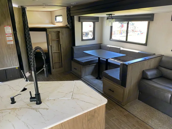 Inside a bright rv rental: modern dining booth, kitchen island, and bunk beds. Perfect for travel comfort.. Forest River Cherokee 2022