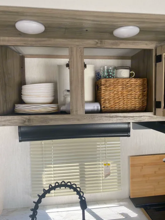 Inside an RV rental, this compact kitchen boasts overhead cabinets with dishes & storage, a modern faucet, and blinds.. Forest River Cherokee 2022