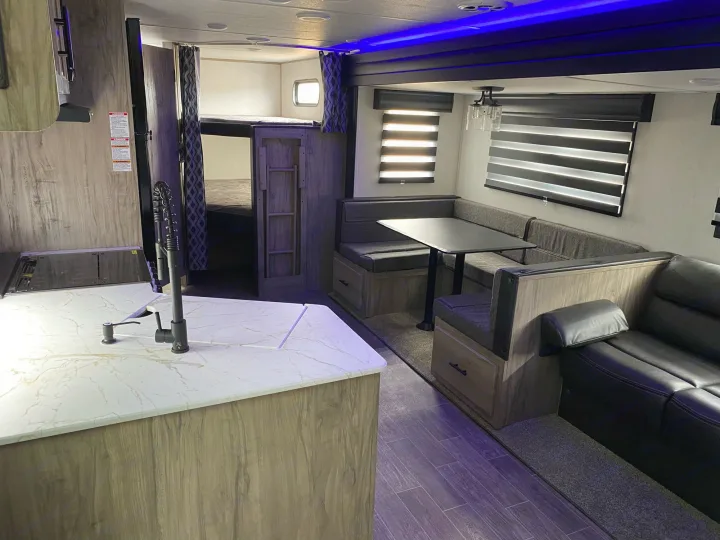 Inside a modern RV rental: kitchen island, dining area, bunk beds, and black sofa. Blue ceiling lights enhance the space.. Forest River Cherokee 2022