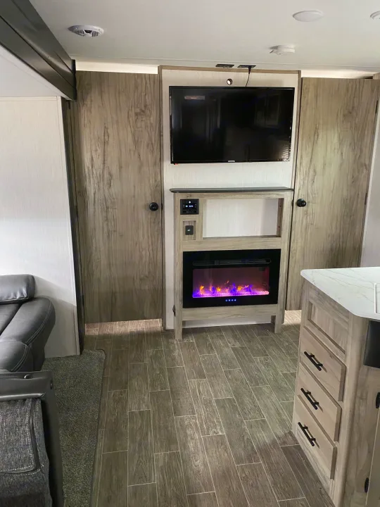 RV rental interior: central entertainment unit with TV & colorful electric fireplace, flanked by storage, and wood-look flooring.. Forest River Cherokee 2022