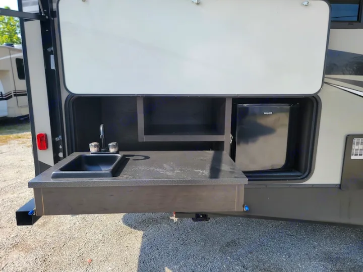 RV rental outdoor kitchen setup featuring a sink, faucet, Hotpoint mini-fridge, and storage shelves. Ideal for camping.. Keystone RV Premier UltraLite 29RKPR 2021