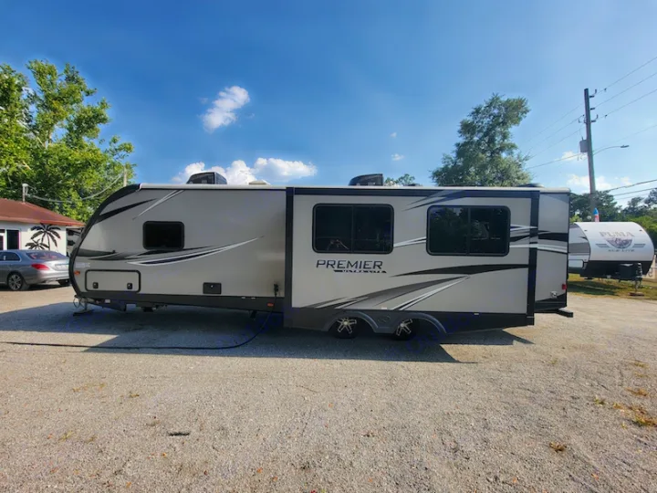 A gray Premier travel trailer RV rental, featuring a slide-out, parked on a sunny gravel lot.. Keystone RV Premier UltraLite 29RKPR 2021