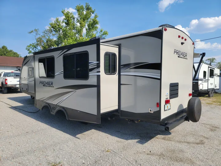 Light gray Premier Ultra Lite RV rental with slide-out extended, parked on a gravel lot under a blue sky.. Keystone RV Premier UltraLite 29RKPR 2021