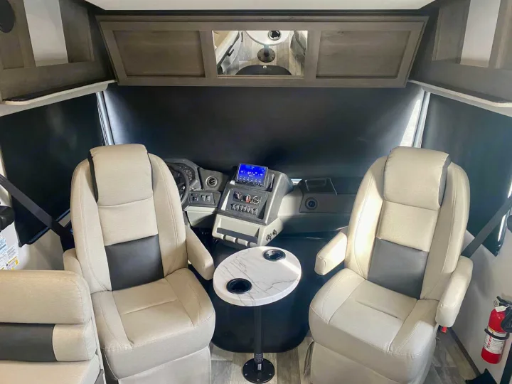Spacious RV rental cockpit featuring comfortable driver & passenger seats, dashboard controls, and a marble-top table.. Forest River FR3 34DL 2020