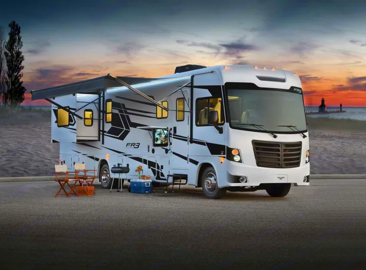 An RV rental is set up for a beachside camping trip at sunset, with an awning, chairs, and grill ready.. Forest River FR3 34DL 2020