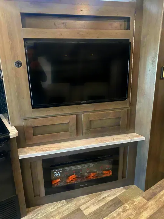 Modern RV rental entertainment center with a large TV mounted above a sleek electric fireplace. Ideal for cozy nights.. Forest River FR3 34DL 2020