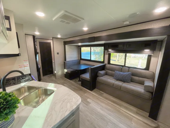 Interior of an RV rental: kitchen, dining booth, and sofa offer comfort. Large windows provide scenic lake & nature views.. Jayco Jay Flight 2022