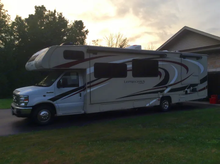 A Class C Coachmen Leprechaun motorhome, an ideal RV rental, is parked on a driveway near a house at dusk.. Forest River Coachmen Leprechaun 2019