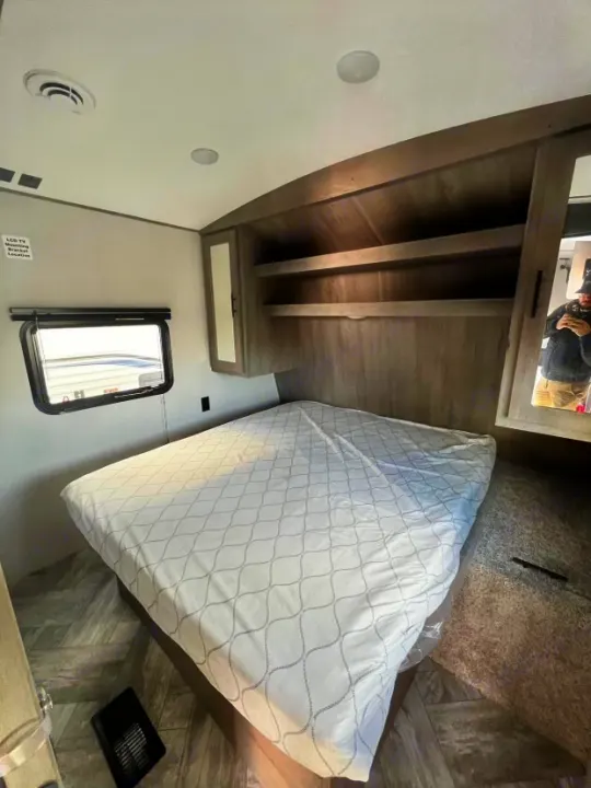 Experience comfort in this RV rental bedroom. Features include a large bed, overhead storage, window, and TV mount.. Keystone RV Springdale 2021