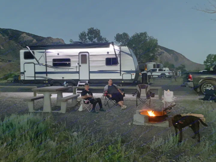 Relaxing RV rental night: Campers by a warm fire, with a large travel trailer and dog at dusk.. Keystone RV Springdale 2021