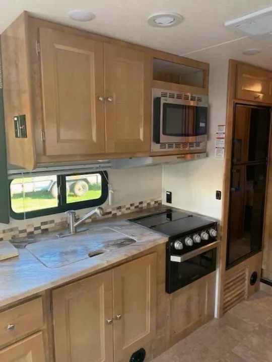 RV rental kitchen: light wood cabinets, microwave, stove, sink, and refrigerator for comfortable travels.. Forest River Coachmen Leprechaun 2019