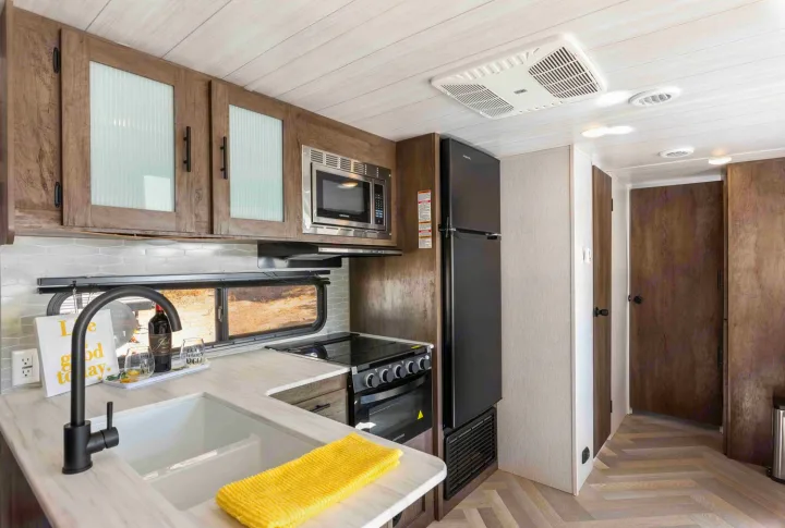 Spacious RV rental kitchen features a black fridge, microwave, stove, deep sink, and wood cabinetry.. Forest River Salem Cruise Lite 2022