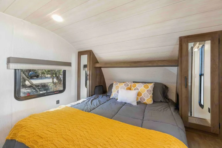 Experience comfort in this modern RV rental bedroom. Features a grey bed with yellow accents, wood ceiling, and a window view.. Forest River Salem Cruise Lite 2022
