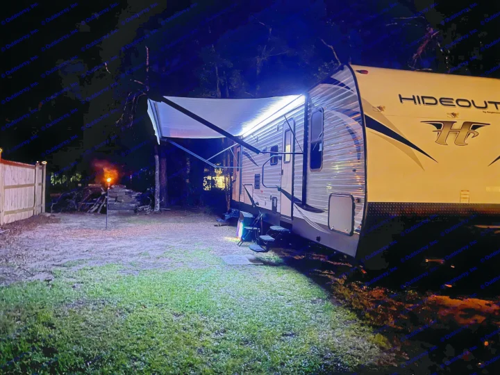 Cozy night setup with an RV rental. Illuminated Hideout camper, extended awning, steps, and grill at campsite.. Keystone RV Hideout 2018