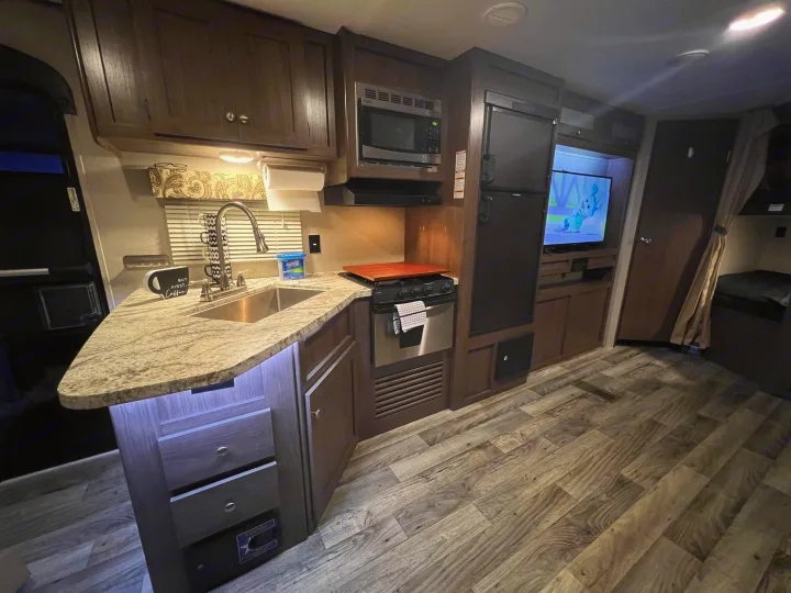 Inside a clean RV rental: kitchen with counter, sink, microwave, stove, fridge, TV, and bunk beds. Ready for travel!. Keystone RV Hideout 2018