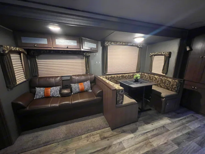 Cozy rv rental interior featuring a brown leather sofa, U-shaped dinette, and wood-look flooring.. Keystone RV Hideout 2018