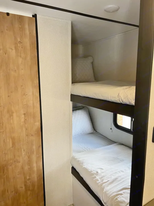RV rental bunk beds: Clean, compact sleeping area with white bedding, perfect for travelers and families.. Keystone Springdale 2022