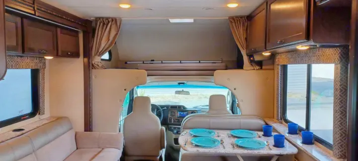 Spacious RV rental interior showing a sofa, set dining table, driver's cab, and overhead bunk.. Thor Motor Coach Four Winds 2018
