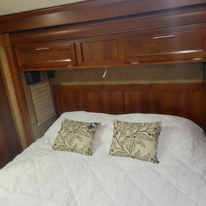 Relax in this cozy RV rental bedroom. Features a large bed with white quilted bedding, patterned pillows & wood overhead storage.. Forest River Fr3 2015