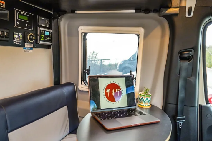 Mobile office setup in an RV rental. Laptop with 'Cruise with Bruce' logo, power controls, seatbelt, and window view.. Winnebago Revel 2022