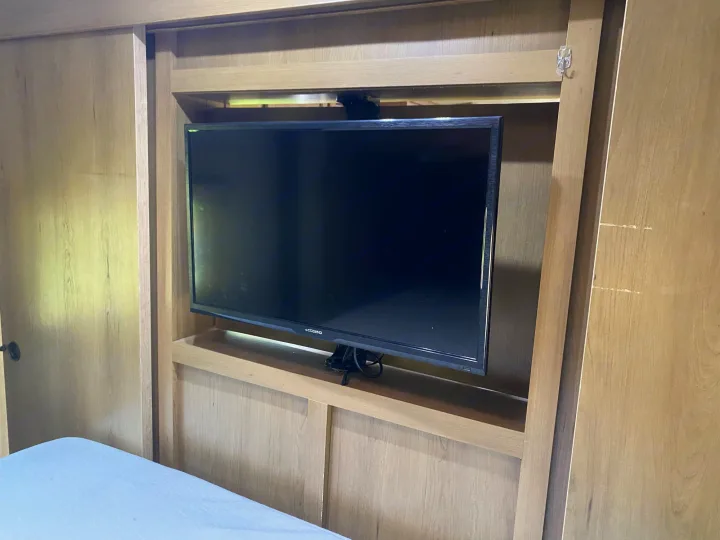 RV rental interior: A TV mounted in a light wood entertainment unit with shelving. Bed and sliding doors are visible.. Cruiser Rv Corp 280Bunkhouse Cruiser 2015