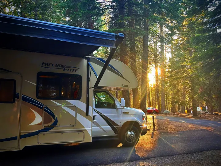 A beige Thor Freedom Elite RV rental parked in a sun-drenched forest campground, perfect for nature getaways.. Thor Freedom Elite 2019