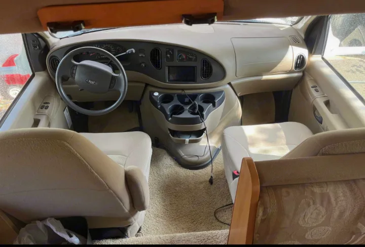 Spacious RV rental interior featuring beige dashboard, steering wheel, captain's chairs, and central console with cup holders.. Winnebago Access 2008