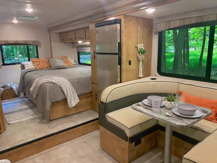 Cozy RV rental interior with a comfortable bed, full-size fridge, and dining area, offering serene views of the surrounding forest.. Forest River Coachmen Leprechaun 2020