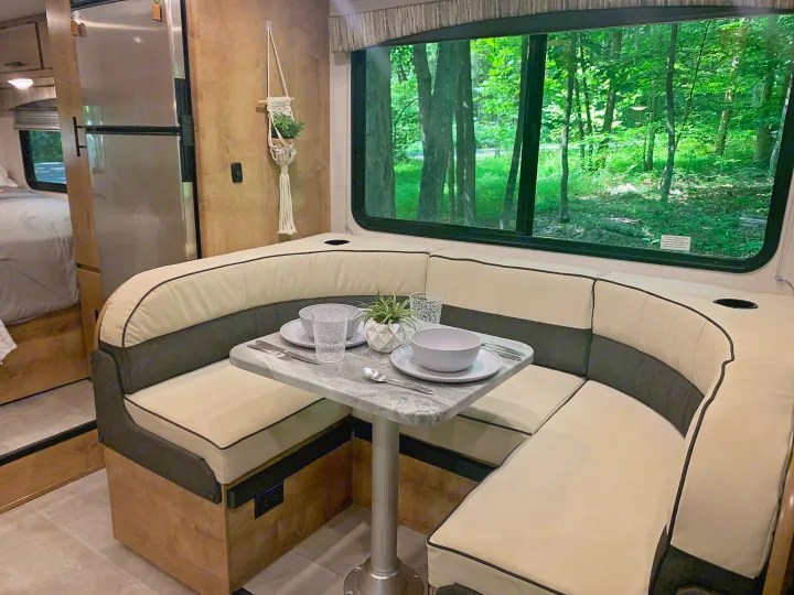 Modern RV rental interior featuring a comfortable U-shaped dining booth with a set table, offering a peaceful forest view.. Forest River Coachmen Leprechaun 2020