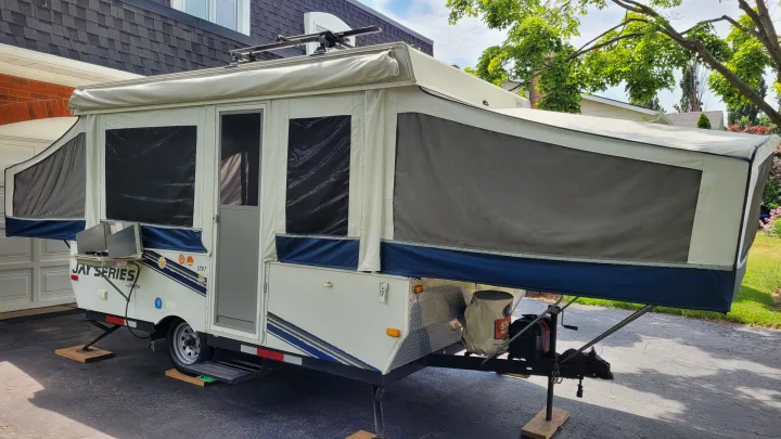 Pop-up RV rental fully set up in a driveway, featuring an outdoor stove and roof rack. Perfect for camping adventures.. Jayco 1207 2008