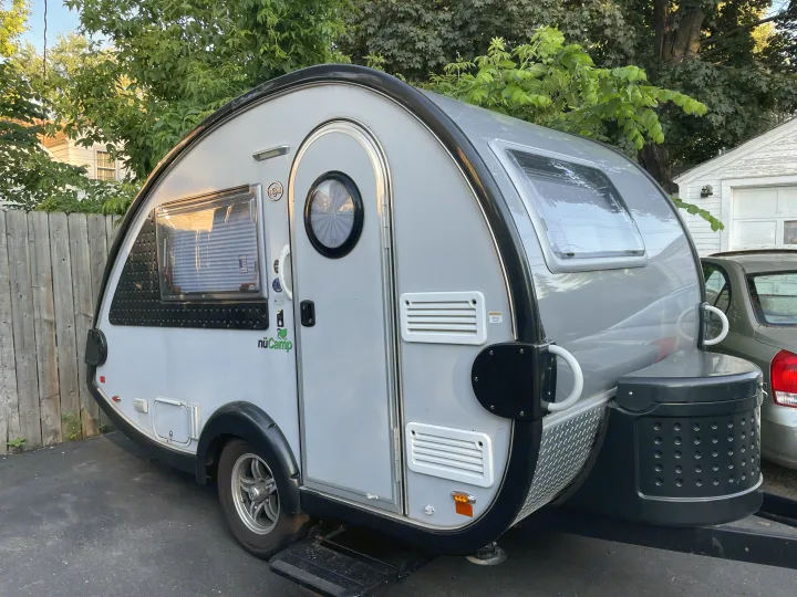 Explore with this nuCamp teardrop RV rental, a compact and modern travel trailer parked near a fence.. nuCamp T@B 2018