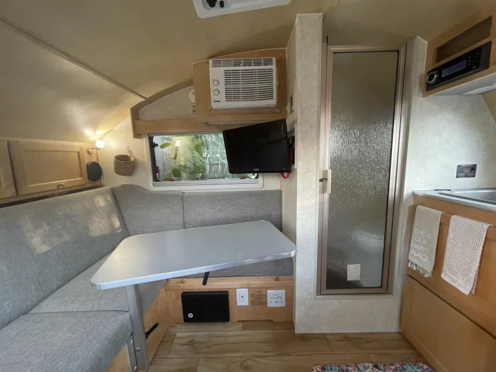 Inside an RV rental: a functional interior with a cozy dinette, compact kitchen, shower stall, AC, and TV.. nuCamp T@B 2018