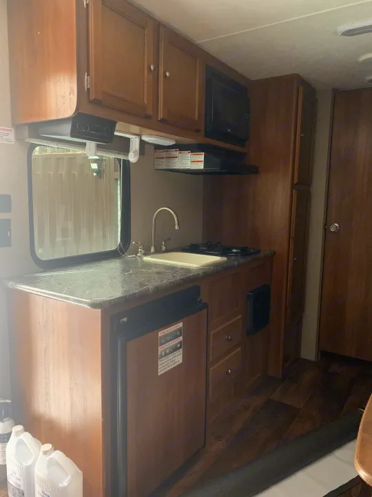 This RV rental features a compact kitchen with wood cabinets, microwave, sink, stove, and refrigerator for functional travel.. Springdale Summit 2017