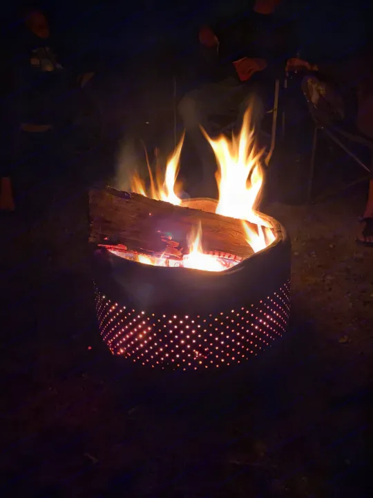 Nighttime campfire in a recycled drum fire pit, casting light on people enjoying an RV rental campsite.. Springdale Summit 2017
