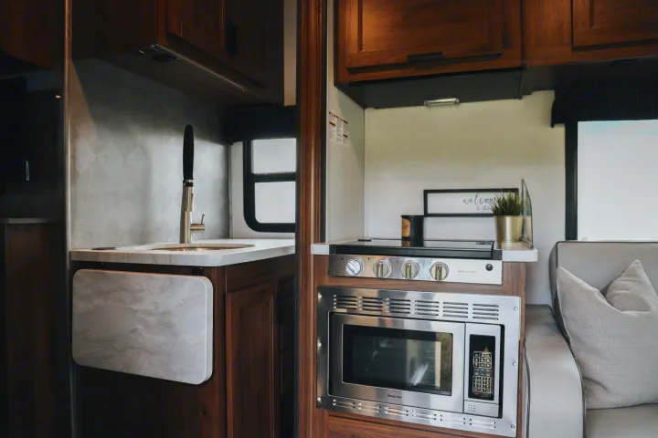 RV rental kitchen: sink with a counter extension, Magic Chef cooktop & microwave, dark wood cabinets.. Forester LE 2021