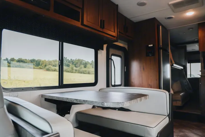 RV rental interior: dinette with table, bench seats, window to nature, and overhead wood cabinets.. Forester LE 2021