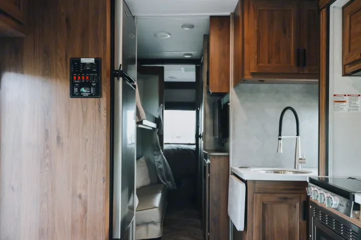 Interior of an RV rental showing a kitchen with sink, stove, wood cabinets, and a control panel on the left wall.. Forester LE 2021