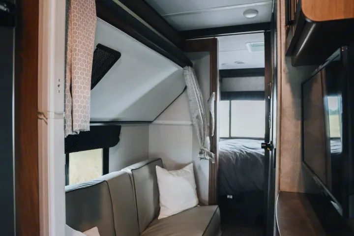 Step inside this modern RV rental: a cozy living space with a sofa, a window view, and a separate bedroom through an open doorway.. Forester LE 2021